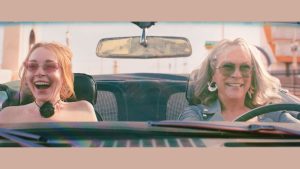 Lindsay Lohan as Anna Coleman (left) and Jamie Lee Curtis as Tess Coleman (right) in Freakier Friday. They are driving in a convertible car, both wearing colorful sunglasses.