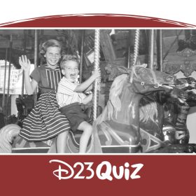 Black and white photo of two children riding King Arthur’s Carrousel at Disneyland Resort. The older girl is wearing a striped dress and waving at the camera, and the younger boy is wearing a striped shirt and dark shorts.
