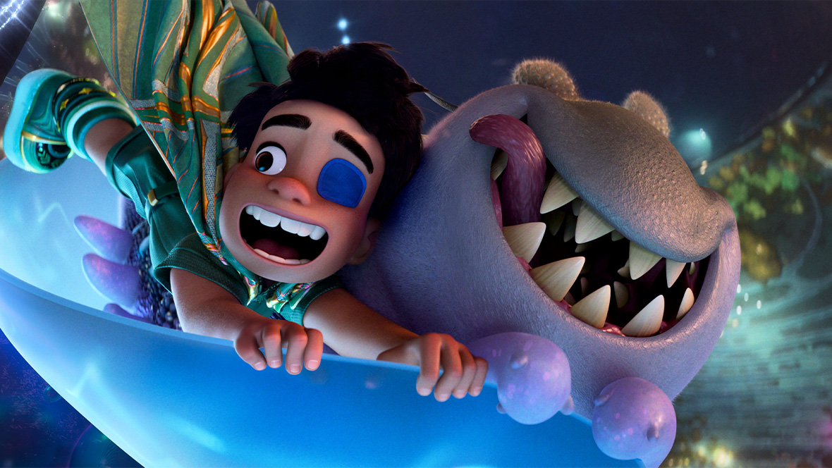 In a still from Disney and Pixar’s Elio, Elio (voiced by Yonas Kibreab), left, and Glordon (voiced by Remy Edgerly), right, are excitedly riding in a light blue cup-shaped vehicle through the Communiverse. They’re holding onto the vehicle for dear life. Elio has a patch over one eye and his mouth is open in a wide smile; Glordon’s tongue is sticking out of one side of his mouth.