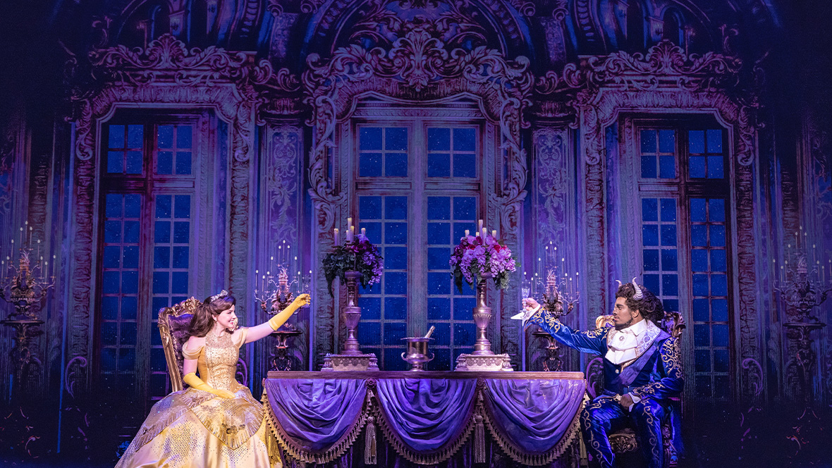 Kyra Belle Johnson as Belle and Fergie L. Philippe as Beast in an exclusive photo from Disney Theatrical Group&rsquo;s North American Tour of Beauty and the Beast. They are seen in the dining room of the Beast&rsquo;s castle; Belle is wearing her iconic yellow ball gown. Both are lifting glasses.