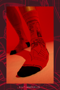 A close-up photo of a pair of red socks being modeled. The red socks are adorned with line art of various Star Wars illustrations including Darth Vader. Where the toes begin within the socks is pure black, and above that is the Stance logo written in black type.