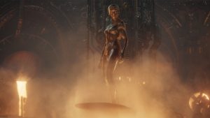 Julia Garner as Shalla-Bal/Silver Surfer in Marvel Studios’ The Fantastic Four: First Steps. She is entirely silver and standing on a surfboard in a cloud of yellow smoke in front of a wall with gears on it.