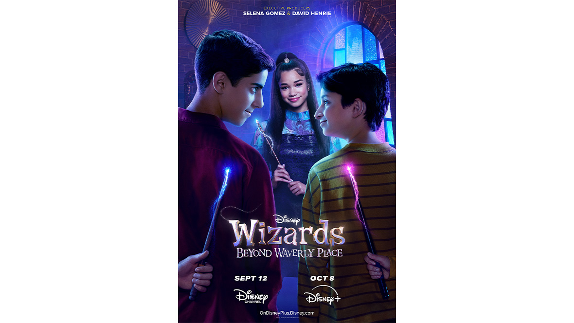 In this studio portrait to promote Disney’s “Wizards Beyond Waverly Place,” pictured is Janice LeAnn Brown, who plays Billie in the show. Her brown hair is styled in two buns on either side of the top of her head, with a few strands hanging on either side of her face She’s wearing a shiny black jacket with a wide collar and a zebra-pattern collarless shirt beneath it. She is seen from the chest up and is smiling with her mouth closed.