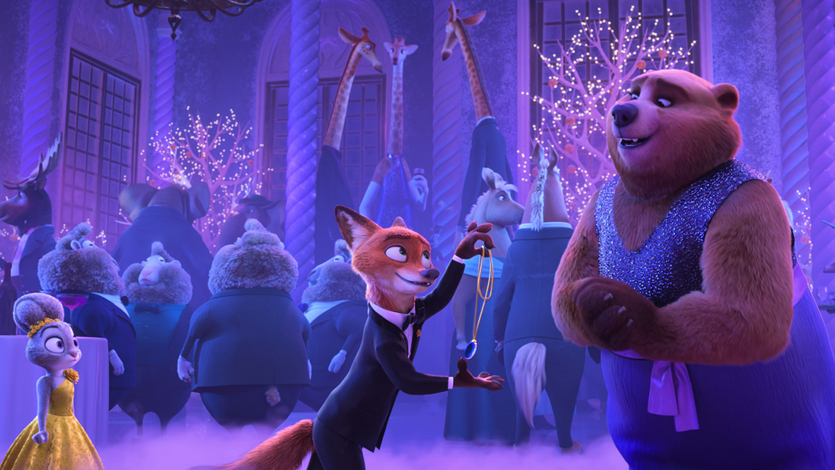 In a scene from Zootopia 2, the fox Nick Wilde, just left of center and wearing a tuxedo, holds up a necklace with a blue gem pendant in front of a smiling bear, just right of center and wearing and blue glitter outfit with a purple sash. Bunny Judy Hopps, wearing a yellow ball gown, stands to the left. Behind these three is a formal party filled with animals in fancy dress and bare trees lit with twinkle lights.
