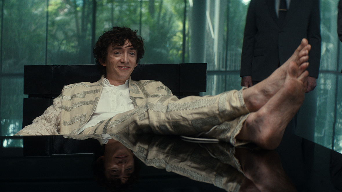 Boy Kavalier (played by Samuel Blenkin) in FX’s Alien: Earth is seen wearing a tan suit with silver embroidery and is sitting with his bare feet propped up on a table.