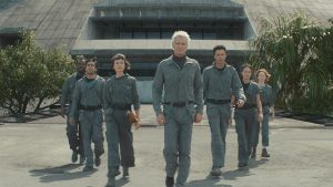 (From left to right) Smee (Jonathan Ajayi), Slightly (Adarsh Gourav), Wendy (Sydney Chandler), Krish (Timothy Olyphant), Tootles (Kit Young), Curly (Erana James), and Nibs (Lily Newmark) from FX’s Alien: Earth are seen walking; they’re wearing matching grey jumpsuits.
