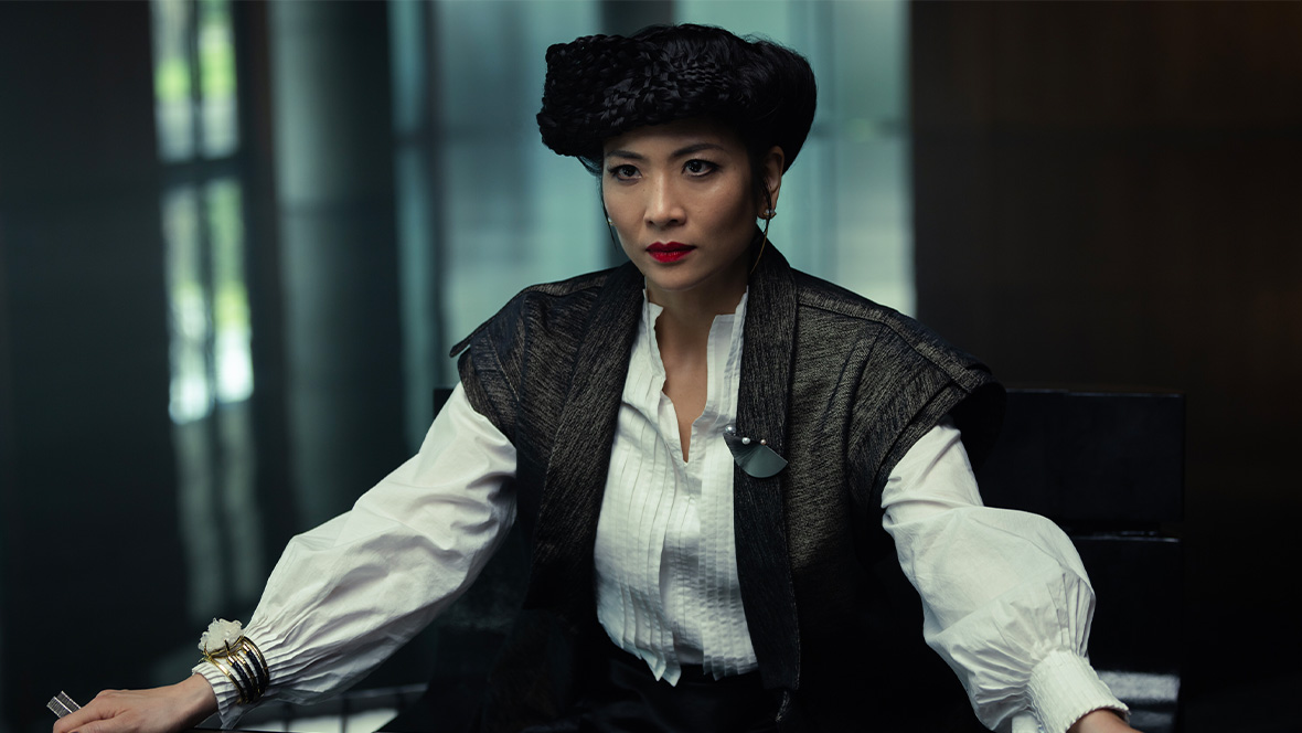 : Yutani (played by Sandra Yi Sencindiver) in FX’s Alien: Earth is sween wearing a white blouse with a futuristic black vest on top. Her hair is woven into elaborate braids worn around her head.