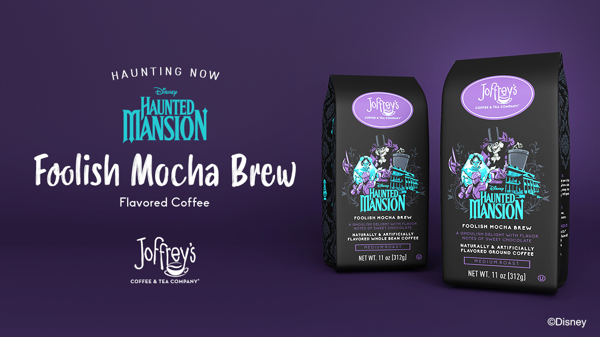 Promotional image for Joffrey’s Coffee & Tea Company’s 'Foolish Mocha Brew,' a Disney Haunted Mansion-inspired flavored coffee. Two black coffee bags with purple Joffrey’s logos are shown, featuring artwork of the Bride, Hatbox Ghost, and the Haunted Mansion in green and purple hues. The coffee is described as a 'ghoulish delight' with sweet chocolate flavor notes. Text reads: 'Haunting Now – Disney Haunted Mansion – Foolish Mocha Brew – Flavored Coffee.