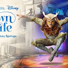 A promotional image for Drawn to Life presented by Cirque du Soleil at Disney Springs in Orlando, Florida. The event text is in a bright blue color, with the show title “Drawn to Life” in a modern stylized font with flowing accents resembling penstrokes. The left side of the image features a hand-drawn theater, with rows of seats sketched by pencil with monochrome shading. The right side of the image transitions from the hand-drawn style into a full color photo of a theater stage. The stage is framed by large pages from a sketchbook with silhouettes of Disney characters—as the image moves from left to right, the sketches move from a hand-drawn style to being in color. In the foreground of the right side of the image is a performer from Drawn to Life. Their arms are spread apart and raised at shoulder height, and legs are crossed whilst jumping. They are leaning forward while wearing a costume evoking an owl, with a green-brown bodysuit with feather accents, and a mask with a small beak and protruding white feathers. The D23 logo is in the upper right corner in white.