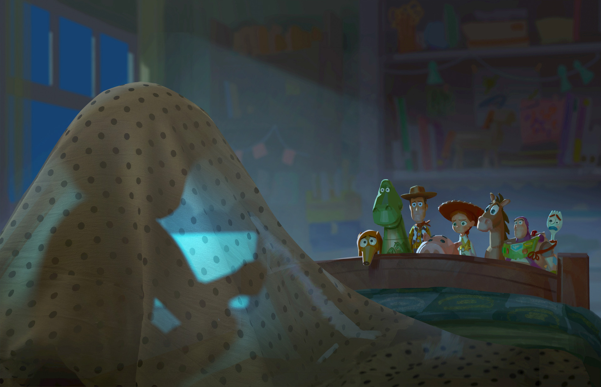 In a scene from Disney and Pixar’s Toy Story 5, we are looking at a darkened bedroom from the head of a twin bed. Directly in front of us, on the left side of the image, a mysterious person, probably a child, is silhouetted beneath a blue polka-dot sheet, holding a computer tablet that has them entranced. At the end of the bed, peeking over the foot of the bed and lit by a beam of moonlight, are many of the Toy Story characters, including Woody, Jessie, and Buzz.