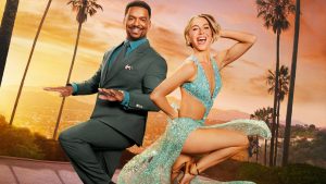 A key art image from Season 34 of ABC’s Dancing with the Stars, featuring hosts Alfonso Ribeiro and Julianne Hough—seen against a sunset sky with palm trees and the ocean in the distance. Ribeiro and Hough are posing as if dancing; Ribeiro is wearing a suit and Hough is wearing a glittery ballroom-style dress
