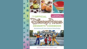 A book cover displays several dessert photos across the top, from left: A pistachio-colored orb of mousse on a chocolate base with what appear to be milk chocolate mouse ears. On the white plate with the mousse are what appear to be cherries in tiny puddles of red glaze. The second photo displays three beignets on a brown plate; both the treats and the plate are powdered with sugar, and a small bowl of what may be chocolate dip is out of focus behind the doughnuts. The third image is a martini glass filled with four or five gelatine-like layers ranging in color from cream to bright red. Stripped down the left side of the book cover is a stripe that faces from green to pink. Along the stripe are silhouetted icons from the Disney Parks, such a Mickey Mouse, a Ferris Wheel, Spaceship Earth, a castle, and so on. At the bottom of the book cover is a photo of Goofy, Donald Duck, Mickey and Minnie Mouse, and Pluto striking a pose in front of Sleeping Beauty Castle at Disneyland Park in Anaheim, California. The text in the middle of the book cover reads: The Official Disney Parks Desserts Cookbook: Remembering 101 Sweet Delicious Disney Recipes, with the author’s name below the park photo: Pam Brandon & The Disney Chefs. A bubble of text above the title promises: Featuring 35 brand-new treats.