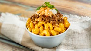 Impossible® Chili Cheese Macaroni and Cheese from the EPCOT International Food & Wine Festival served in a small, white bowl placed on top of a brown and white towel on a wooden countertop.