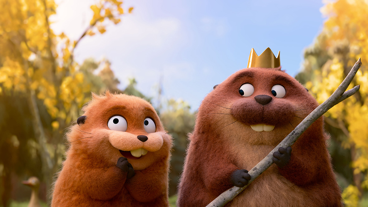: In a scene from Disney and Pixar’s upcoming original animated film Hoppers, two beavers are seen from the chest up, standing on their hind legs. The beaver on the left has orange-tan fur and a sly smile on its face. The beaver on the right is slightly larger with darker brown fur and a tan chest. That beaver is looking down and to the right at the smaller beaver. The larger beaver wears a small gold crown and holds a stick as if it were a scepter. Behind the beavers are trees with autumn leaves.