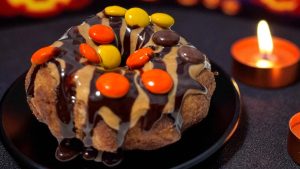 A churro donut rolled in chocolate sugar, drizzled with peanut butter and chocolate sauce, and topped with peanut butter chocolate candy pieces from Sunshine Churros in Disney Springs Marketplace.