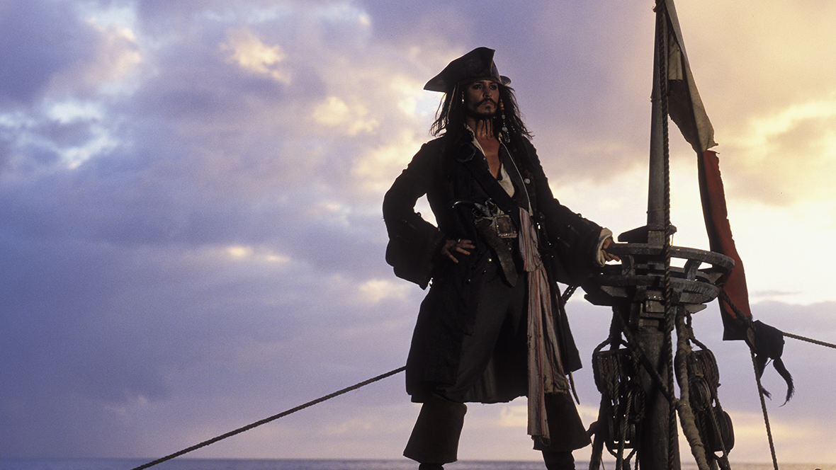 Captain Jack Sparrow (played by Johnny Depp) standing on a ship during sunset in a still from Pirates of the Caribbean: The Curse of the Black Pearl.