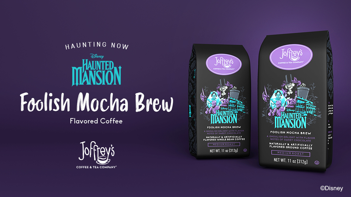 Two bags of Disney Haunted Mansion Foolish Mocha Brew coffee grounds are seen on the right, each featuring an image of The Haunted Mansion attraction, the Hatbox Ghost, the Bride, and a suit of armor. Text on the left reads “Haunting Now. Disney Haunted Mansion Foolish Mocha Brew Flavored Coffee. Joffrey’s Coffee & Tea Company.” Images and text are set against a dark purple backdrop.
