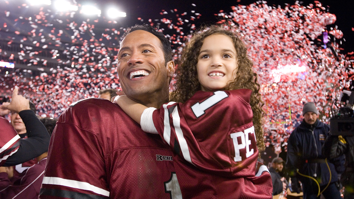 (From left to right) Joe Kingman (played by Dwayne “The Rock” Johnson) holding Peyton Kelly (played by Madison Pettis) in a still from The Game Plan.