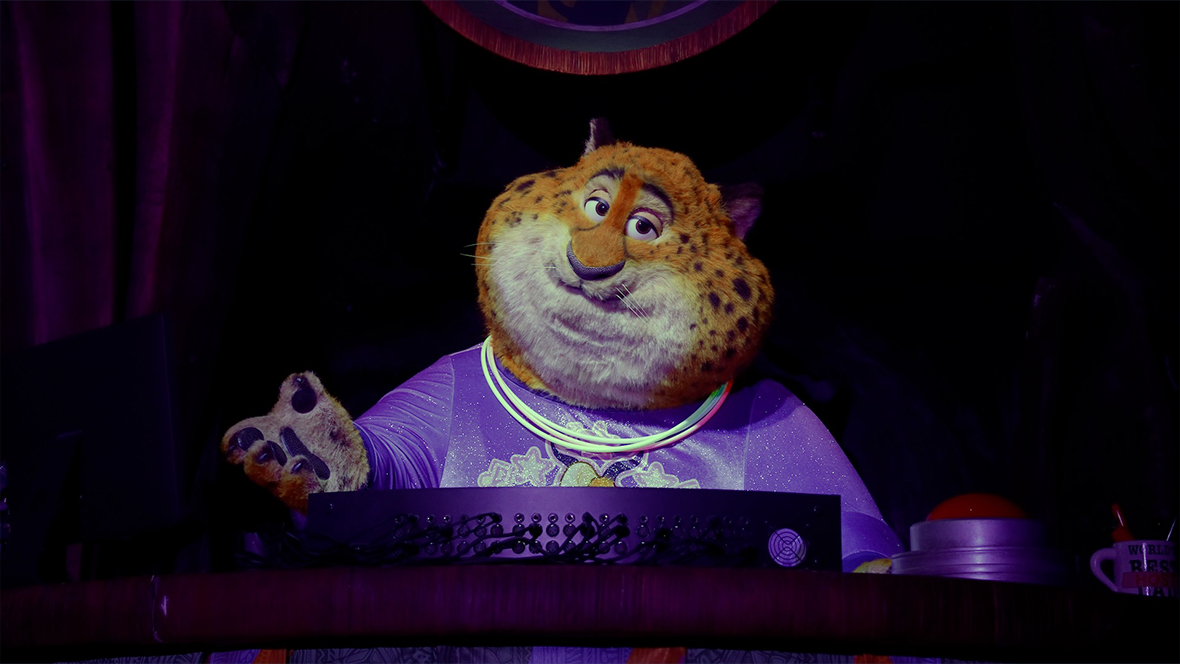 An image of the new Benjamin Clawhauser Audio-Animatronics figure for the Zootopia: Better Zoogether! show at Disney’s Animal Kingdom Theme Park. He’s sitting behind a desk and console of some kind, including a computer monitor. Above him is a Tree of Life-style logo featuring other Zootopia characters.