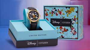 The Soaring High Mickey Mouse watch is displayed upright in a teal and black box. Text on the teal part of the box reads “Limited Edition”; the black bottom portion of the box showcases the silver Disney and Citizen logos, separated by a thin silver line. Behind this watch display is the top of the box featuring hand-drawn versions of previous Macy’s Thanksgiving Day Parade balloons, including Mickey Mouse, Pluto, Donald Duck, and Minnie Mouse. Also stamped on this boxtop is the Disney and Citizen logos separated by a thin silver line.