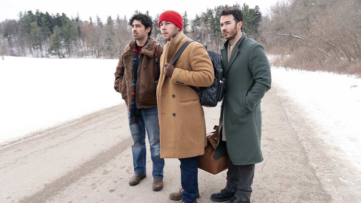 From left to right, Joe Jonas, Nick Jonas, and Kevin Jonas — all wearing winter clothing — stand on a snow-covered road in a scene from A Very Jonas Christmas Movie.