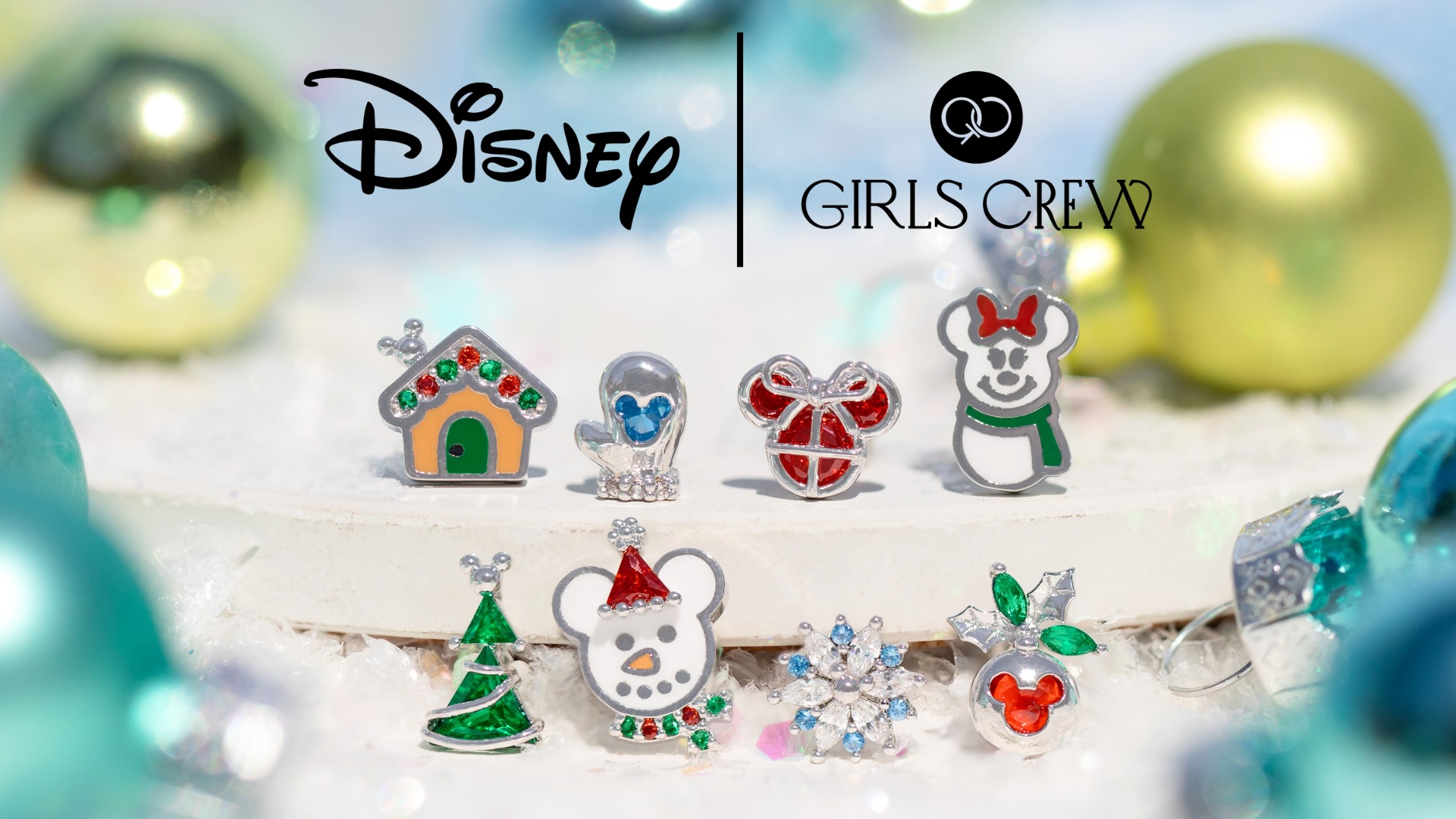 Graphic featuring eight assorted earrings, including a gingerbread house, a snowman in the Minnie Mouse shape, a tree ornament with the Mickey Mouse logo, and more. They are set against a winter landscape with full-size ornaments scattered throughout. The top of the image showcases the Disney logo and Girls Crew logo, separated by a black line.