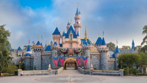 An image of Sleeping Beauty Castle at Disneyland Park, decorated for the Disneyland Resort 70th Celebration. In the front of the castle is a multicolored crest featuring the number &ldquo;70&rdquo;; leading up to the castle are blue and pink flags with gold trim. Each flag also includes the &ldquo;70&rdquo; crest.