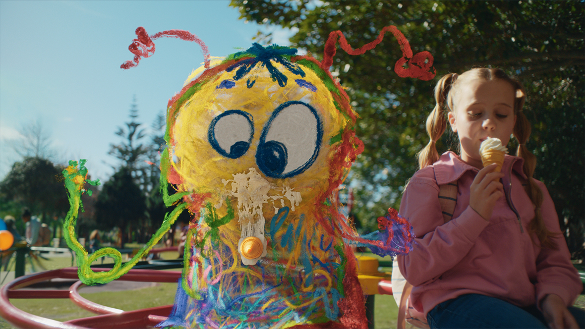 A still from A Disney Holiday Short: Best Christmas Ever, directed by Taika Waititi and featuring the voice of Disney Legend John Goodman. In it, a little girl and a doodle that has come to life are sitting next to each other outside; the girl is eating an ice cream cone.