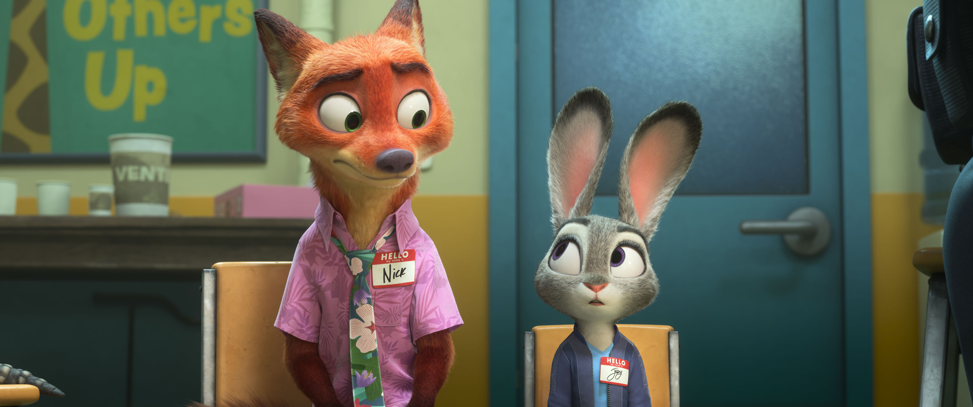 In an image from Walt Disney Animation Studios’ Zootopia 2, Nick Wilde (voiced by Jason Bateman), left, and Judy Hopps (voiced by Ginnifer Goodwin), right, are sitting in an office and wearing name tags that display their first names. Nick is wearing a Hawaiian shirt and a loud tie; Judy is a plain blue sweater and light-colored shirt.