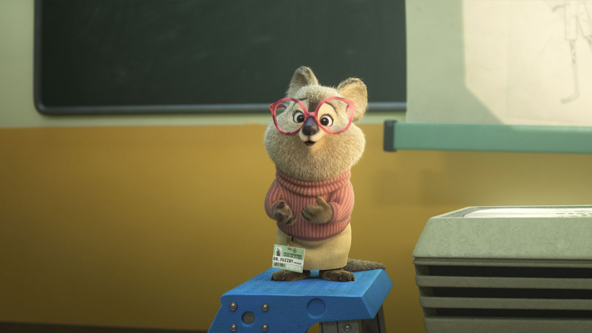 A still from Walt Disney Animation Studios’ Zootopia 2 features Dr. Fuzzby (voiced by Quinta Brunson), a small marsupial wearing big pink glasses. She’s standing on top of a ladder to the left of a projector and screen, on which appears an image of two animals.