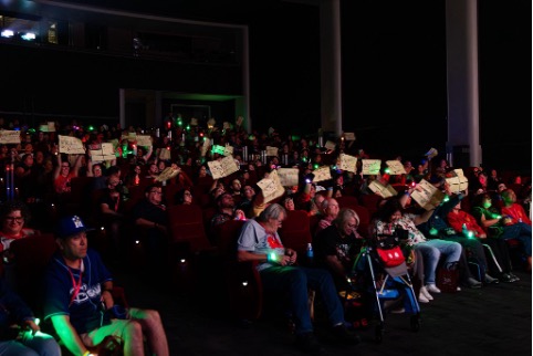 An audience in a dark theater watching Home Alone; most people are holding up their copies of Kevin’s Battle Plan and wearing light-up wristbands.