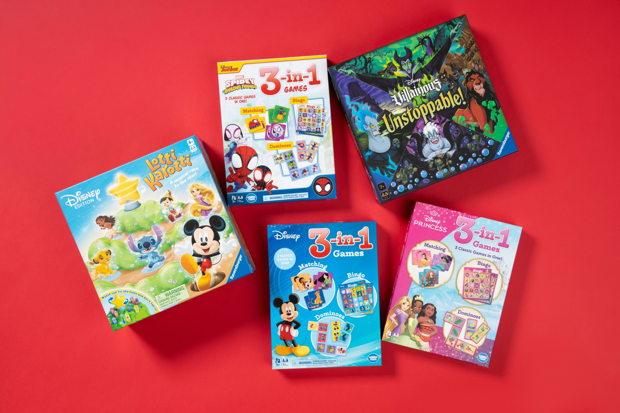 Assorted Ravensburger games are scattered in front of a red background. These games are all Disney-themed and feature characters such as Mickey Mouse, Disney Villains, Spider-Man, and Disney Princesses. Some of the packages advertise 3-in-1 card games, while others are board games.