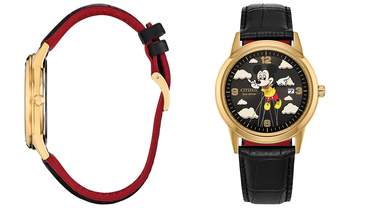 An image of the Soaring High Mickey Mouse watch. The dial of the watch is black with clouds surrounding the edges; at center is the Mickey Mouse Macy’s Thanksgiving Day Parade Balloon being held down with strings. Mickey’s white-gloved hands move around the dial as the “hands” of the watch. The dial also includes the “Citizen Eco-Drive” logo and a date window. The watch case is a gold, with a black leather strap.
