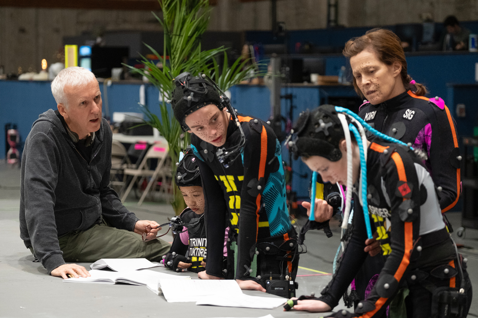 A behind-the-scenes image from the making of 20th Century Studios&rsquo; Avatar: Fire and Ash; director James Cameron, left, is seen working with Trinity Jo-Li Bliss, Britain Dalton, Jack Champion, and Sigourney Weaver on the set.