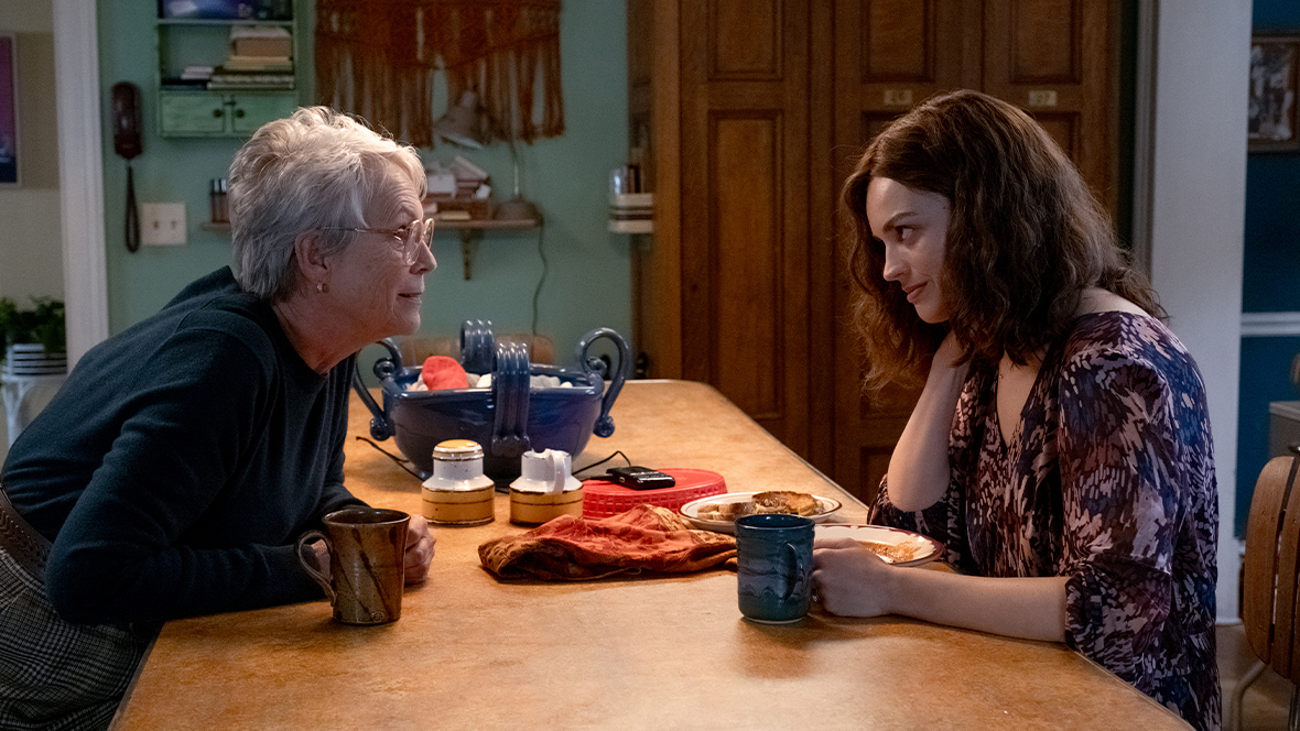 In an image from 20th Century Studios’ Ella McCay, Disney Legend Jamie Lee Curtis as Helen, left, and Emma Mackey as Ella, right, sit at a kitchen dining table. They have cups and plates of food in front of them, and appear to be in the middle of a conversation.