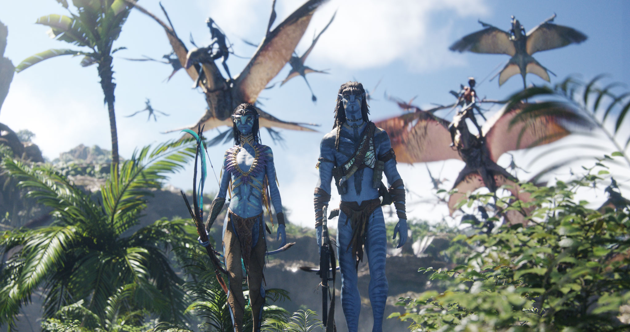 In an image from 20th Century Studios&rsquo; Avatar: Fire and Ash, Neytiri (Zoe Salda&ntilde;a), left, and Jake Sully (Sam Worthington), right, are walking through a jungle scene as other warriors on flying creatures swirl around them in the sky.