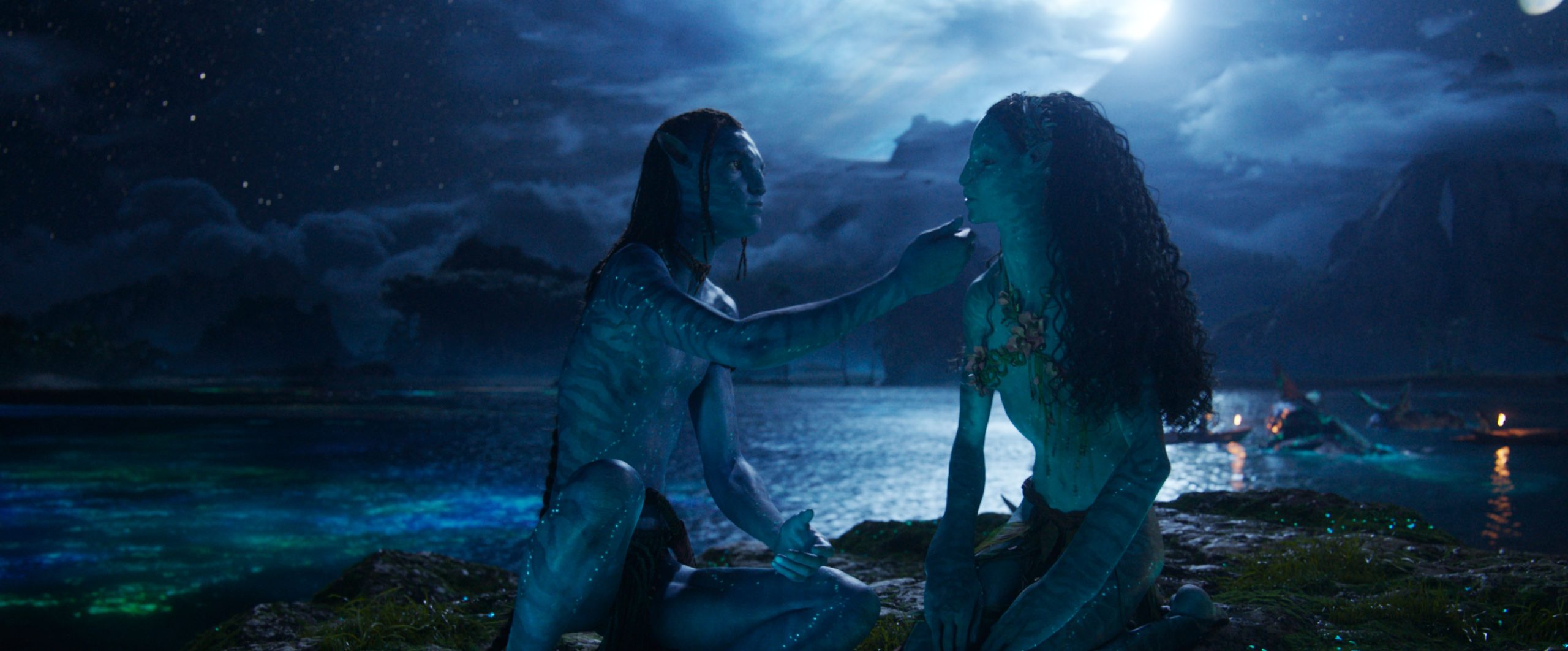 In an image from 20th Century Studios&rsquo; Avatar: Fire and Ash, Lo&rsquo;ak (Britain Dalton), left, and Tsireya (Bailey Bass), right, are sitting next to each other in the moonlight, near the water. Lo&rsquo;ak is gently touching Tsireya&rsquo;s face.