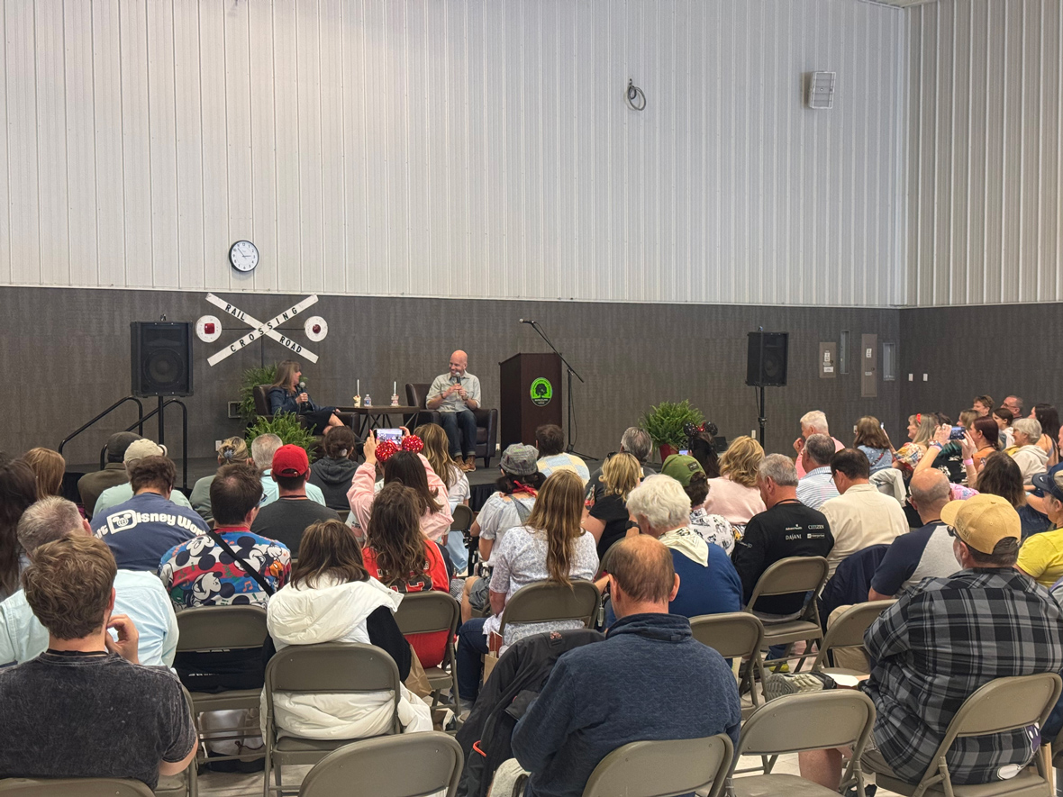 Image from the May 2025 D23 event in Marceline, Missouri, Walt Disney&rsquo;s boyhood home. Brent Iwan, voice of Mickey Mouse, speaks to a host in front of a crowd.
