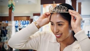 A woman in the Arribas Brothers store places a tiara atop her head. The tiara frame is gold and covered in rhinestones. She sports other jewelry including gold earrings and a gold watch band.