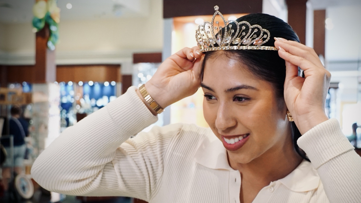 A woman in the Arribas Brothers store places a tiara atop her head. The tiara frame is gold and covered in rhinestones. She sports other jewelry including gold earrings and a gold watch band.