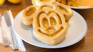 A Mickey shaped waffle sits on a plate from the free hot breakfast area at Drury Plaza Hotel Orlando &ndash; Disney Springs Area, with potatoes and fruit in the background.