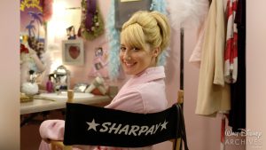 Sharpay (Ashley Tisdale) sits in a personalized director&rsquo;s chair in her dressing room before performing the song &ldquo;Bop to the Top.&rdquo; She is in a pink robe with a bedazzled collar. The background of the picture features Sharpay&rsquo;s clothes, accessories, and makeup desk.