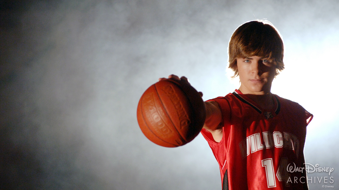 In a publicity photo for High School Musical, Troy Bolton (Zac Efron) is wearing a red and black basketball jersey with white lettering that reads &ldquo;Wildcats&rdquo; and a number 14 on the center of his chest. He is holding a basketball in front of the camera and is 