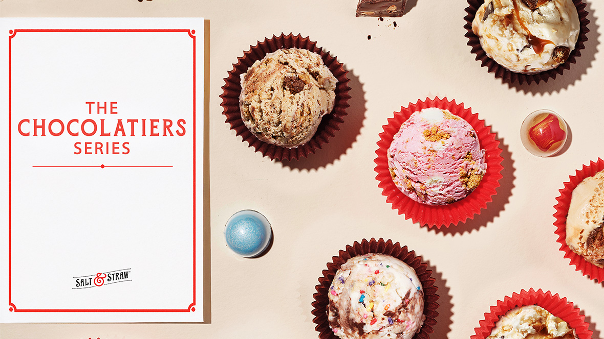 Promotional display for Salt & Straw's "The Chocolatiers Series" featuring scoops of artisanal ice cream in red and brown cups, styled like truffles with mix-ins such as chocolate chunks, caramel swirls, cookie pieces, and sprinkles. A white card with red border displays the series name, alongside two spherical candies in blue and red.