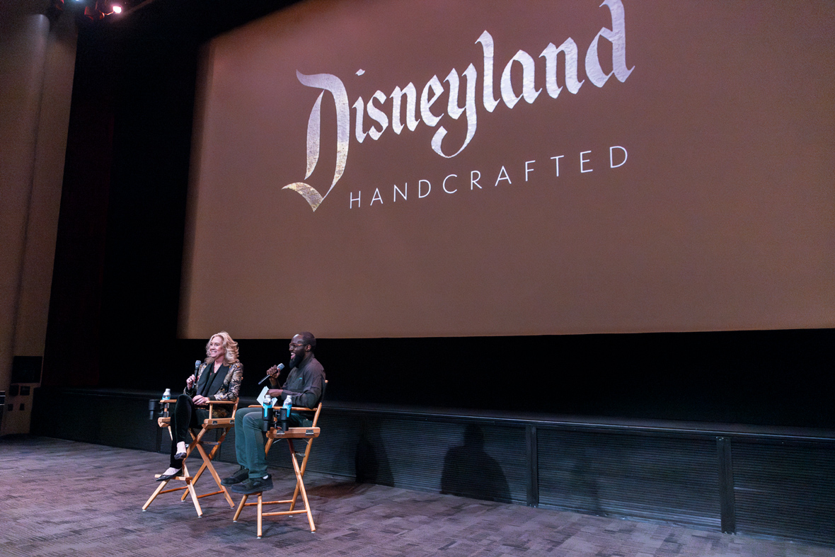Leslie Iwerks (left) and Juju Green (right) sit in director&rsquo;s chairs under the screen at the Walt Disney Studios&rsquo; Main Theater doing a Q&A before the premiere screening of Iwerks&rsquo; documentary film Disneyland Handcrafted. Both are holding microphones and smiling. The film&rsquo;s logo can be seen on the screen above and behind them.