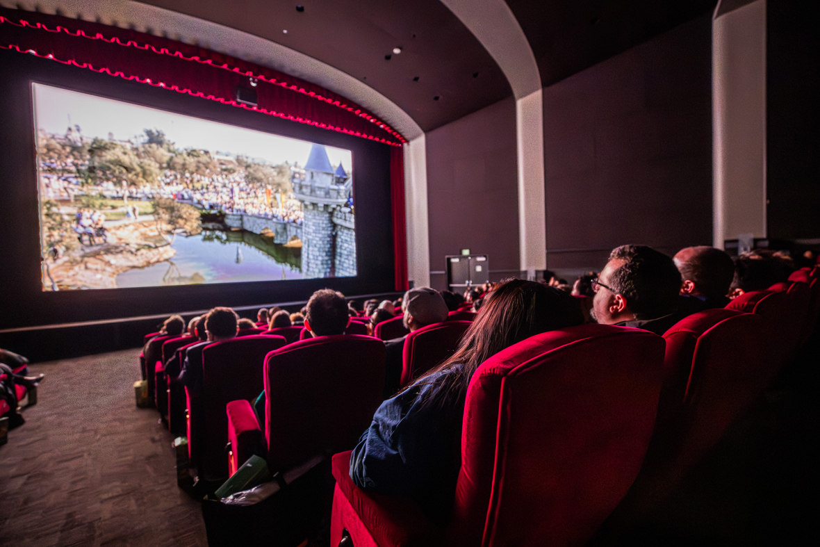 An image from inside the Walt Disney Studios&rsquo; Main Theater as the invited audience watches Leslie Iwerks&rsquo; documentary Disneyland Handcrafted. The film is playing on the screen, and audience members can be seen&mdash;illuminated by the screen&mdash;in the foreground.