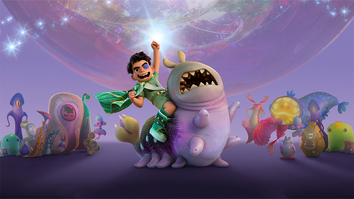 A young boy named Elio, who is wearing an eye patch, green clothes, and a sparkling green cape, sits on the back of Glordon, a large, purple alien with a wide, toothy smile and multiple stubby legs. Elio is smiling wide and has one fist raised high. Elio and Glordon are surrounded by several bizarre and colorful alien creatures of various shapes.