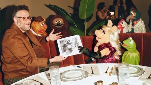 Seth Rogen, left, sits with Miss Piggy, middle, and Kermit the Frog, right, at a table booth inside the Hollywood Roosevelt during the Muppet Show premiere event on January 31, 2026. Miss Piggy is handing Rogen a signed headshot. Behind the trio are, left to right, Fozzie Bear, Rowlf the Dog, Camilla the chicken, and Gonzo the Great.