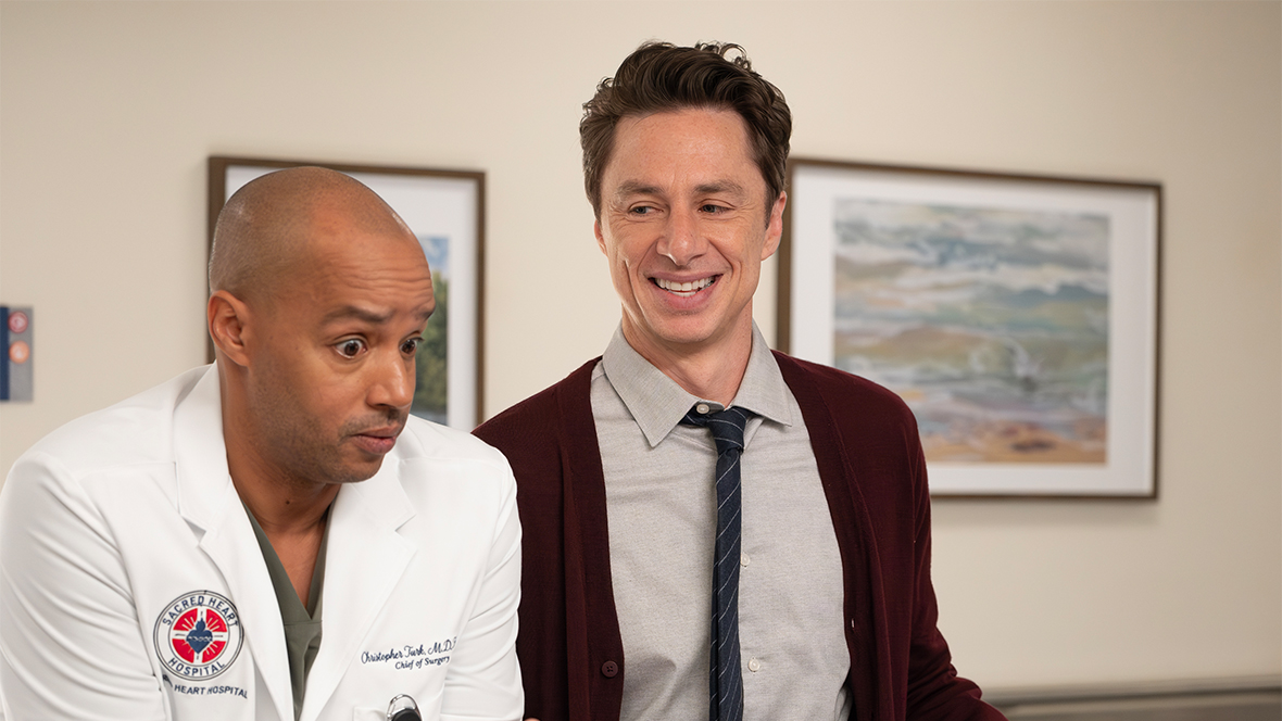 In an image from ABC&rsquo;s Scrubs, Turk (Donald Faison), left, and J.D. (Zach Braff), right, are standing at a nurses&rsquo; station counter. Turk is wearing a lab coat, and J.D. is wearing a maroon sweater, grey button-up shirt, and dark striped tie.