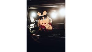 Two images side by side, from the Muppet Show premiere event at the Hollywood Roosevelt in Los Angeles on January 31, 2026. On the left, Miss Piggy is looking out of a limousine window as camera flashes go off; she is raising sunglasses above her eyes. On the right, Kermit and Miss Piggy sit at a table booth and are being offered a slice of strawberry pie; behind them, Fozzie Bear (to Kermit&rsquo;s left) and Rowlf the Dog (to Miss Piggy&rsquo;s right) look on. There are various place settings and a white tablecloth on the table.